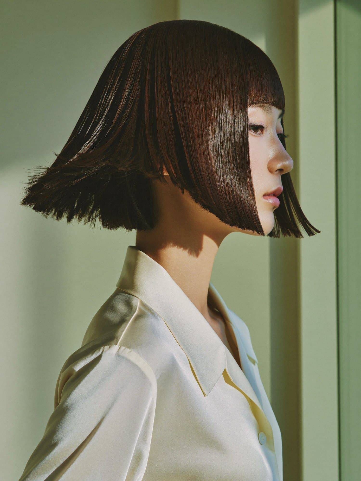A profile of a woman with a sharp espresso-brown bob and fringe.