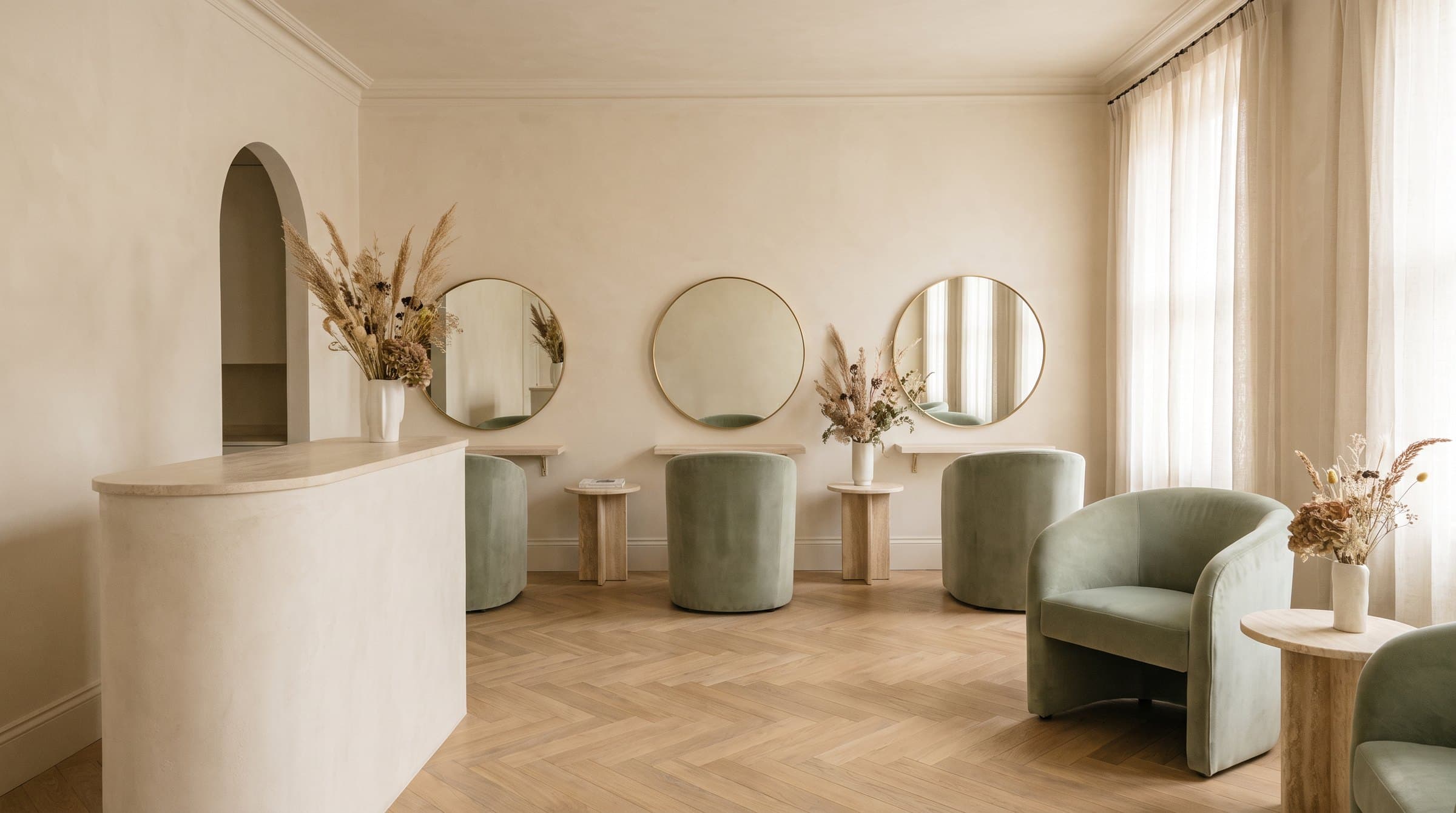 A Georgian townhouse salon with round brass mirrors, sage velvet chairs and a curved limestone reception desk.