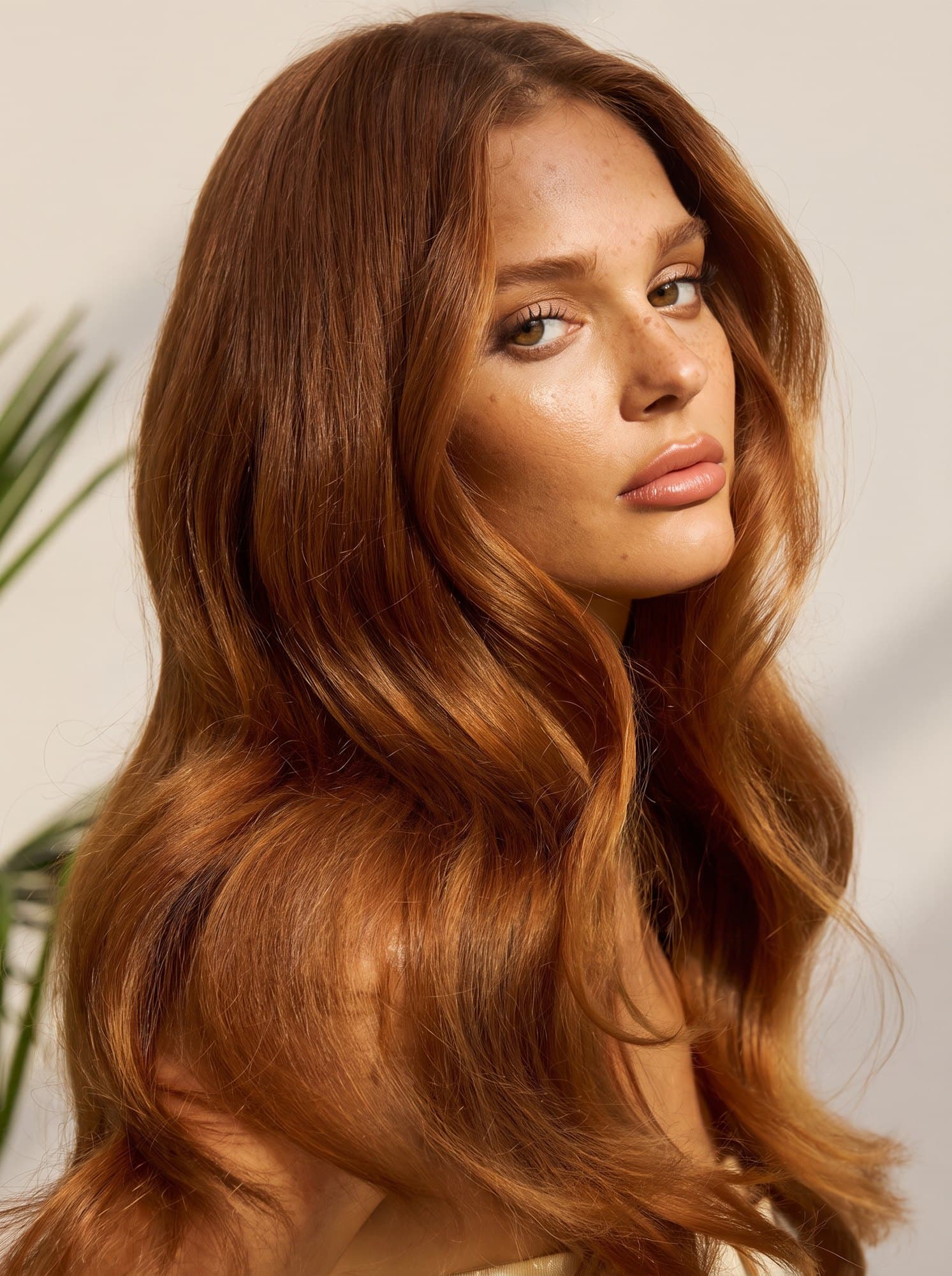 A woman with long, polished copper-auburn waves looking over her shoulder.
