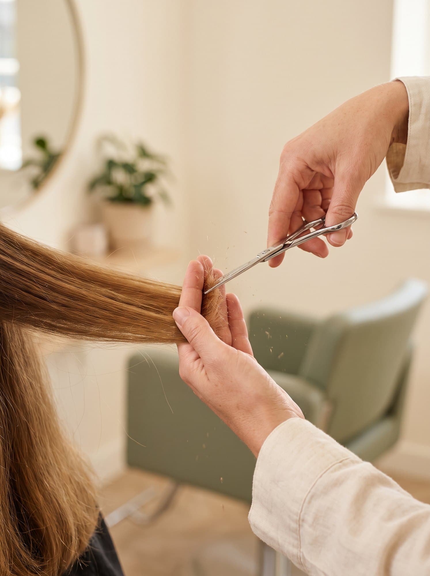 A stylist precision-cutting a section of honey-brown hair with scissors.
