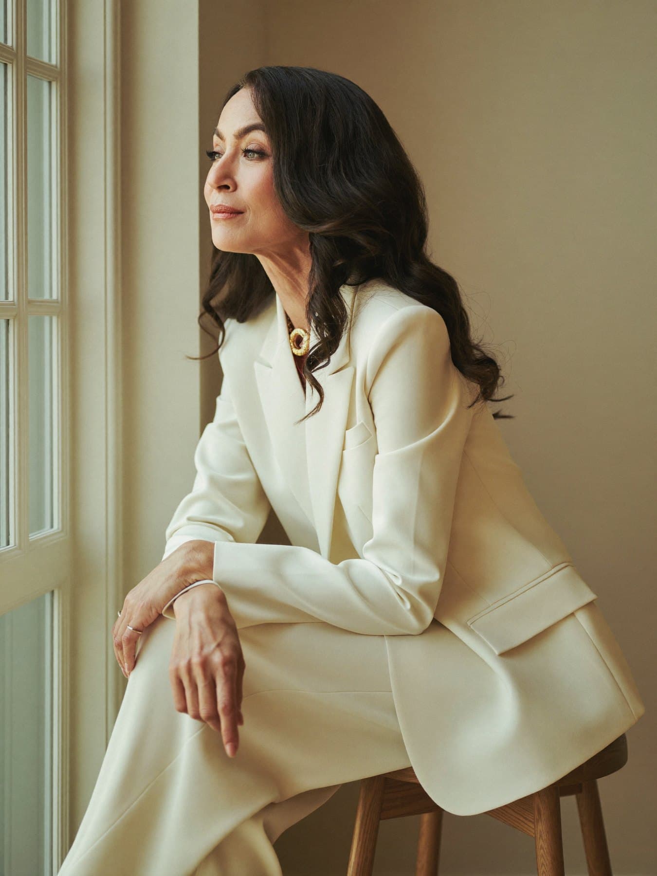 Portrait of Anjali, a stylist in a cream blazer, seated by a window.