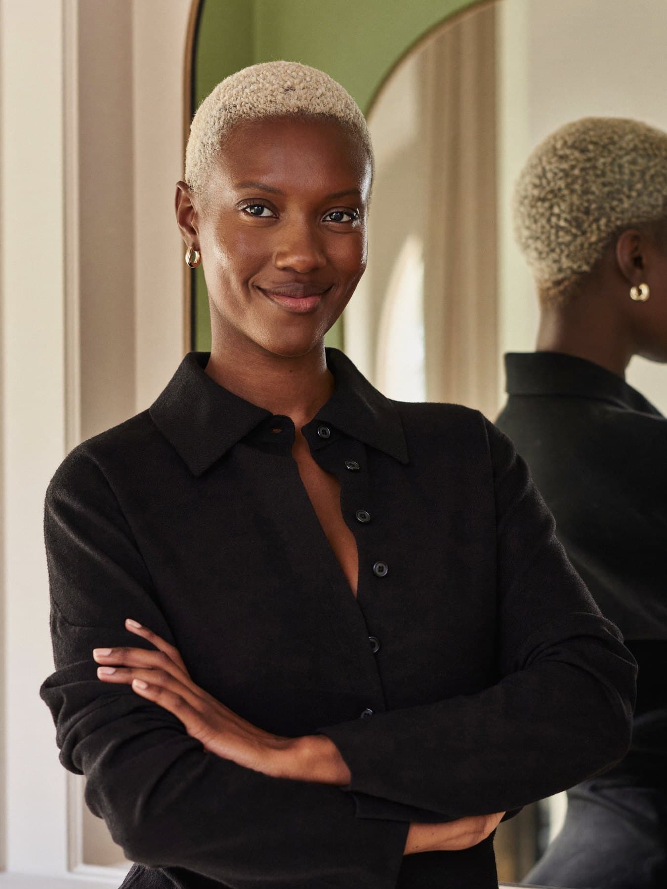 Portrait of Nia, a colourist with a platinum crop, arms folded and smiling.
