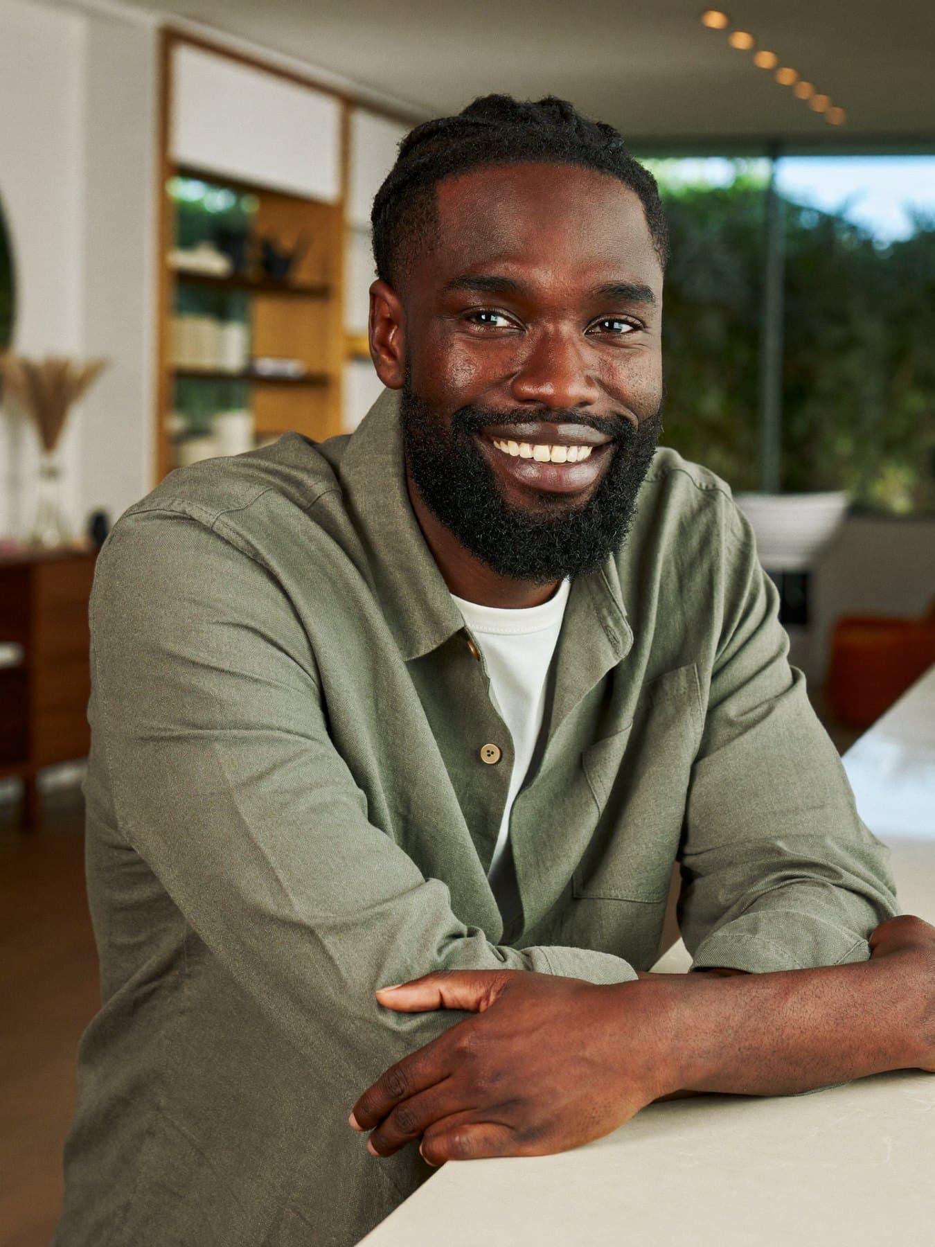 Portrait of Theo, a stylist in a sage linen shirt, smiling at a limestone counter.